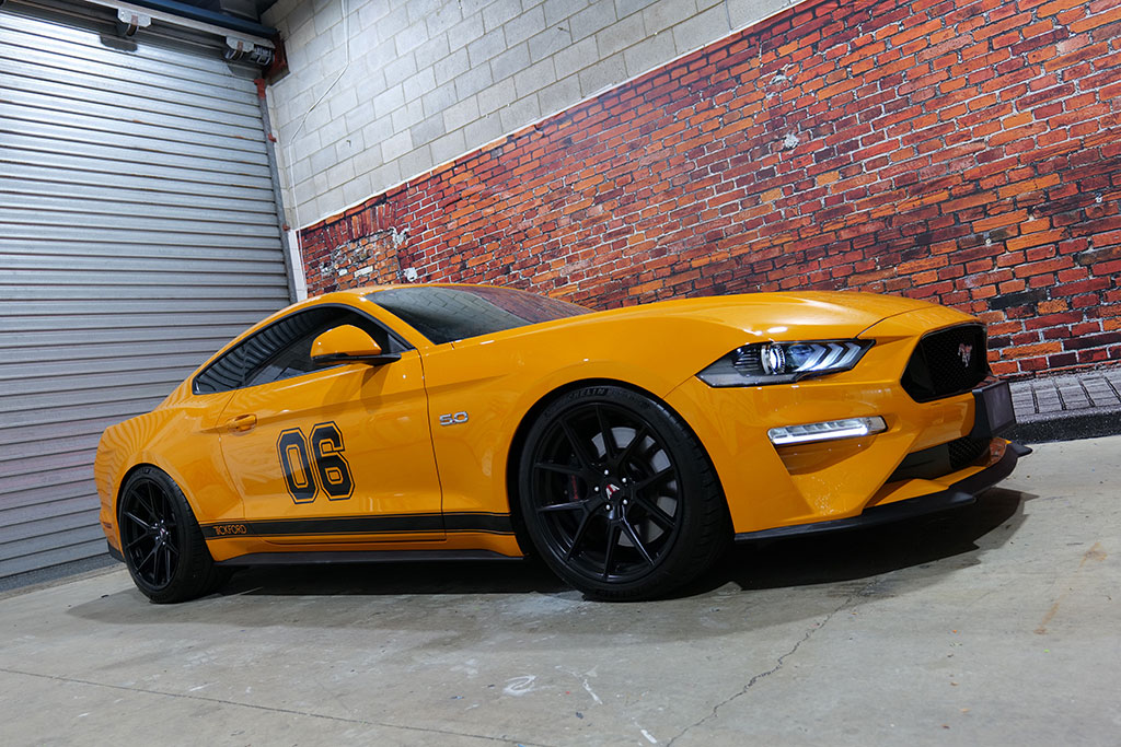 Yellow Ford Mustang GT 5.0 with black ‘06’ race-stripe vinyl wrap at Omega Graphix garage